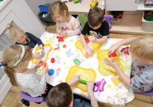 Dzieci siedzące pry stoliku lepiące z ciastoliny.