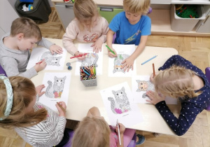 Dzieci siedzące przy stoliku kolorujące mandale - koty.