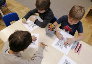 Dzieci siedzące przy stoliku kolorujące mandale - koty.