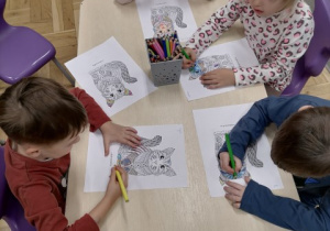 Dzieci siedzące przy stoliku kolorujące mandale - koty.