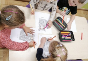 Dzieci siedzące przy stoliku kolorujące mandale - koty.