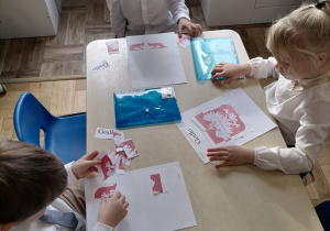 Grupa dzieci przy stoliku układająca godło Polski.