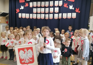 Grupa dzieci w strojach galowych śpiewająca hymn.