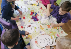 Grupa dzieci siedząca przy stoliku wycinająca cyfrę 6.