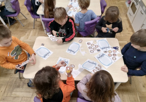 Dzieci siedzące przy stoliku i wycinające obrazki z głoską T.