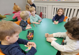 Dzieci siedzące przy stoliku wykonujące pracę plastyczną.