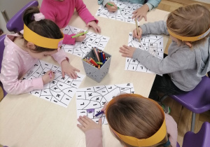 Grupa dzieci siedząca przy stoliku kolorująca pracę.