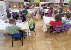 Dzieci siedzące przy stoliku kolorujące pracę.