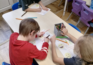 Dzieci wykonujące pracę plastyczną przy stoliku.