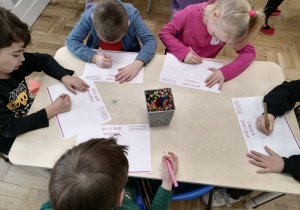 Dzieci wykonujące pracę plastyczną przy stoliku.