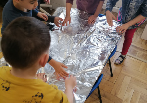 Dzieci bawiące się lodem i śniegiem na folii aluminiowej.