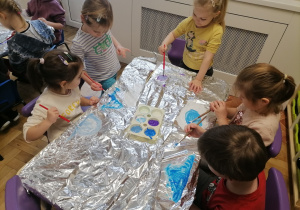 Dzieci malujące farbami po folii aluminiowej.