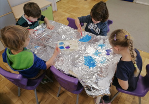 Dzieci malujące farbami po folii aluminiowej.