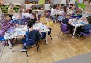 Dzieci malujące farbami po folii aluminiowej.