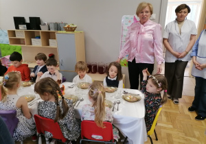 Dzieci w eleganckich strojach siedzące przy wielkanocnym stole.