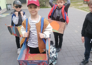 Dzieci w ogrodzie przedszkolnym w wykonanych przez siebie kartonowych autach.
