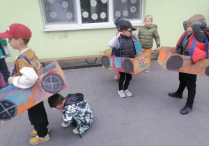 Dzieci w ogrodzie przedszkolnym w wykonanych przez siebie kartonowych autach.