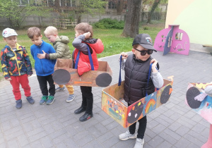 Dzieci w ogrodzie przedszkolnym w wykonanych przez siebie kartonowych autach.