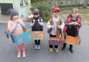 Dzieci w ogrodzie przedszkolnym w wykonanych przez siebie kartonowych autach.