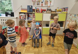 Chłopiec w papierowej koronie siedzący na krzesełku, dookoła niego stoją dzieci.