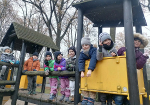 Dzieci pozują do zdjęcia stojąc na drewnianym zestawie ogrodowym