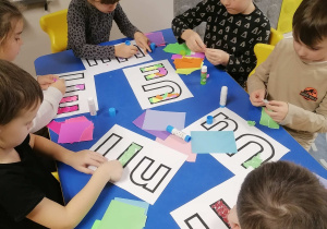 Dzieci przy stoliku wyklejają kolorowym papierem kontury litery U