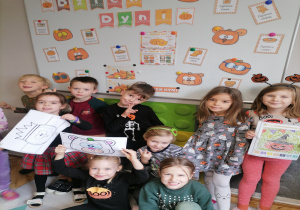 Dzieci pozują do zdjęcia z kolorowankai na tle dekoracji z okazji Dnia dyni