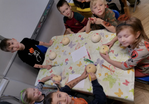 Dzieci siedzą przy stoliku z białymi dyniami