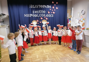 Dzieci w strojach biało czerwonych machają flagami podczas uroczystości