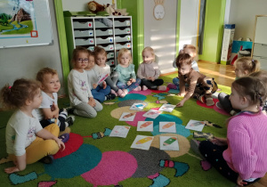 Dzieci siedzą na dywanie z planszami kolorowych kredek