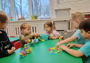 Dzieci siedzą przy stoliku i układają klocki