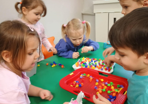 Dzieci siedzą przy stoliku i układają mozaikę