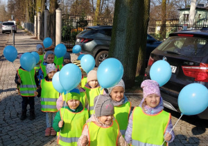Dzieci w odblaskowych kamizelkach spacerują z niebieskimi balonami