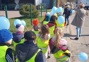 Dzieci w odblaskowych kamizelkach idą z niebieskimi balonami