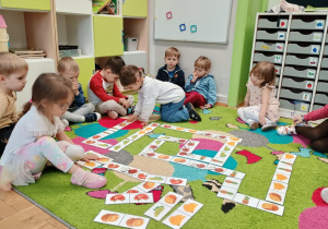 Dzieci układają na dywanie owocowe domino