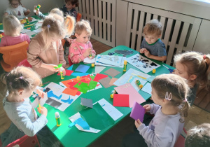 Dzieci wycinają nożyczkami kolorowy papier i przyklejają do kartki papieru