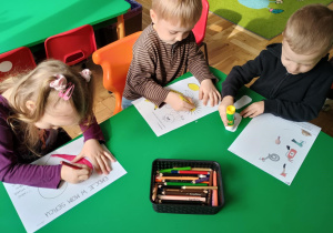 Dziewczynka i dwóch chłopców uzupełniają karty pracy