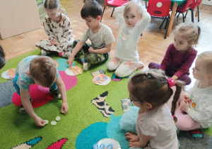 Dzieci siedzą na dywanie i przeliczają papierowe jajka
