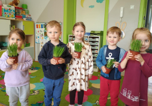 Dzieci pozują do zdjęcia trzymając owies w doniczce