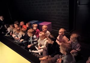 Dzieci siedzą a poduszkach i oglądają przedstawienie teatralne