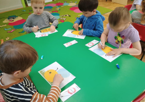 Dzieci siedzą przy stoliku i rysują szlaczki na rysunku pszczoły