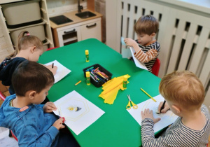 Dzieci siedzą przy stoliku i wykonują pracę plastyczną