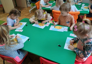Dzieci siedzą przy stoliku i rysują szlaczki na rysunku pszczoły