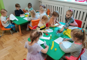 Dzieci siedzą przy stoliku i wykonują pracę plastyczną