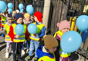 Dzieci wraz z niebieskimi balonami spacerują nieopodal przedszkolu w związku z Dniem Świadomości Autyzmu.