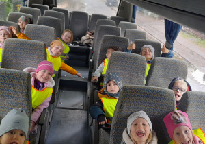 Grupa dzieci w odblaskowych kamizelkach siedzi w autobusie.