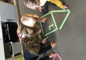 Trójka dzieci układająca domek z kolorowych pasków papieru.