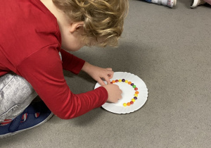 Chłopiec układający kolorowe cukierki na talerzu.