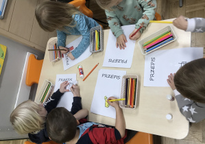 Dzieci siedzące przy stoliku i kolorujące kredkami obrazek koktajlu owocowego.