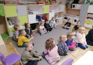 Grupa przedszkolna siedząca na dywanie.